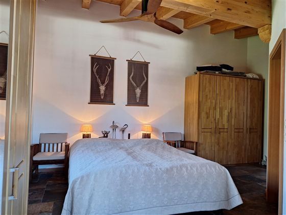 Een gezellige slaapkamer met een groot bed en houten meubels. Aan de muren hangen decoratieve foto's, en de verlichting is warm en uitnodigend.