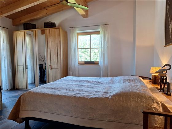 Een heldere slaapkamer met een groot bed en houten details. De kamer heeft grote ramen die veel daglicht binnenlaten.