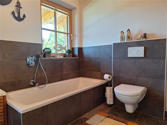 Een moderne badkamer met een bad en een toilet. De wanden zijn in neutrale kleuren gehouden en er zijn ramen met veel natuurlijk licht.