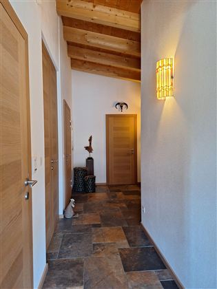 Een lichte gang met houten plafonds en stenen vloertegels. Meerdere deuren en decoratieve elementen creëren een uitnodigende sfeer.