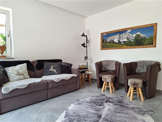 Een moderne woonkamer met een comfortabele bank en twee stoelen. Aan de muur hangt een schilderij met berglandschap.