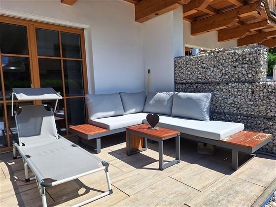 Een gezellige terras met een zithoek en een ligstoel. De meubels zijn modern en nodigen uit om te ontspannen.