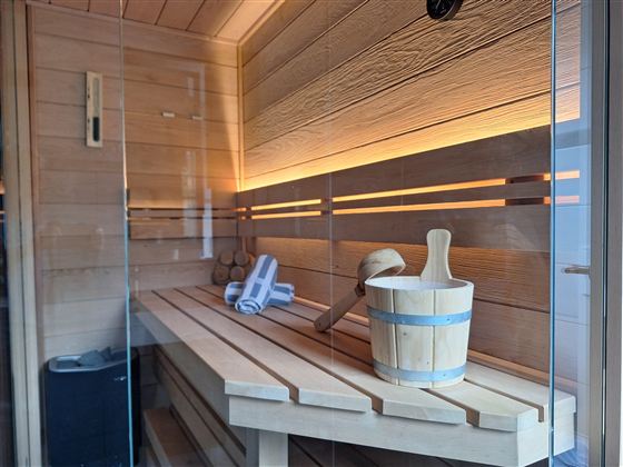 Eine moderne Sauna mit Holzverkleidung und sanfter Beleuchtung. Ein Holzbehälter mit einem Handtuch und einem kleinen Besen steht bereit.