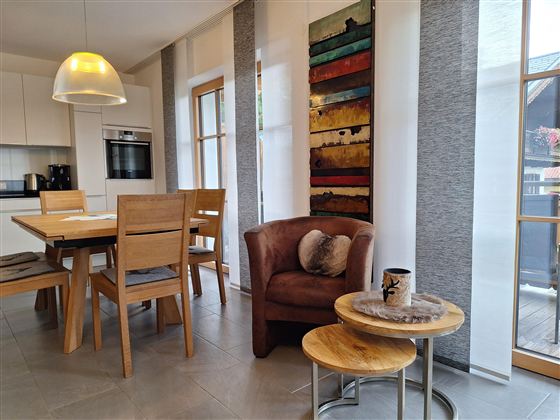 Ein moderner Essbereich mit einem Holztisch und Stühlen. Ein bequemer Sessel und ein kunstvolles Wandbild ergänzen die gemütliche Atmosphäre.