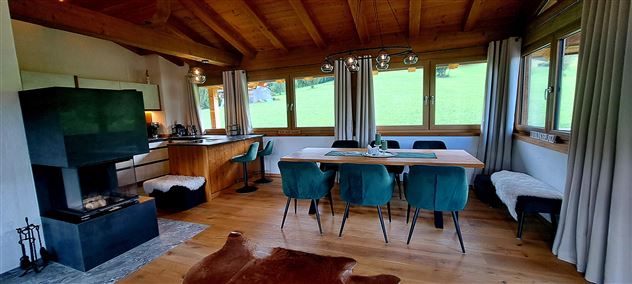 Een gezellige eetruimte in een houten huis met grote ramen en uitzicht op groen. De ruimte is modern ingericht met een eettafel en stijlvolle stoelen.