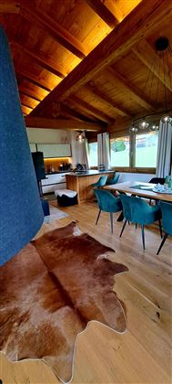 Een moderne, uitnodigende eetkamer met houten balkenplafond. Stijlvolle meubels en een koeienvel zorgen voor een gezellige sfeer.