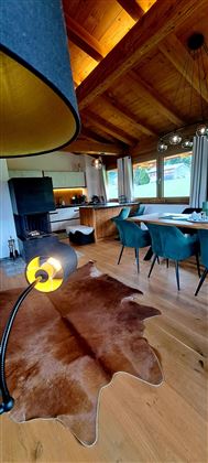 Een moderne woonkamer met houten balkenplafond en grote ramen. Er is een stijlvolle eettafel en comfortabele stoelen, evenals een leren tapijt.
