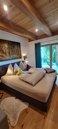 Een gezellige slaapkamer met een groot bed en veel kussens. Grote ramen bieden uitzicht op de groene natuur.