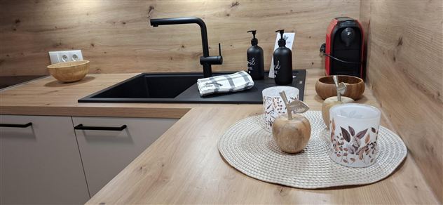 A modern kitchenette with wooden surfaces and minimalist furnishings. On the table, there are decorative items such as a bowl, candles, and a coffee machine.