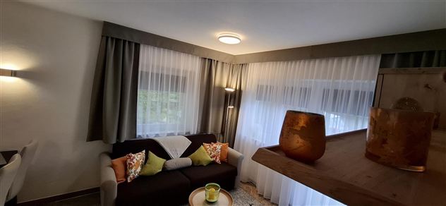 A cozy living room with a sofa and colorful cushions. Large windows let in plenty of light and create an inviting atmosphere.