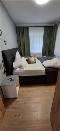 A cozy bedroom with a double bed and large windows. The walls are in soft colors, and there is hardwood flooring.