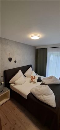 A cozy bedroom with a large bed and modern pillows. The walls are kept neutral, and a window provides daylight.