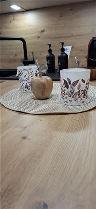 A beautiful set table with a round placemat. On the table are two decorative cups and a small wooden apple.