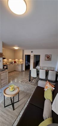 A modern living room with an open kitchen and a dining area. The decor is bright and inviting with a comfortable sofa and a small table.