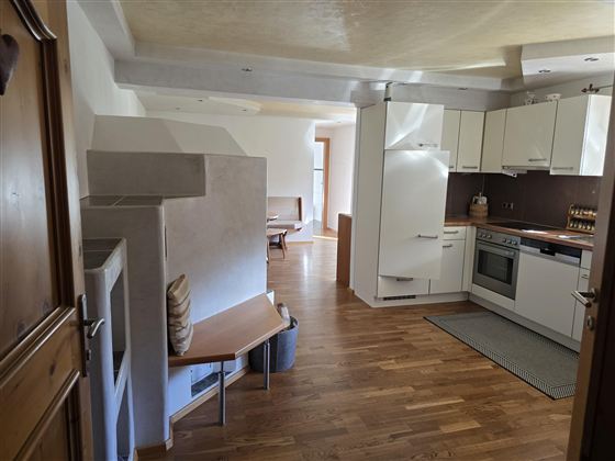 Een moderne keuken met houten vloeren, kasten en moderne apparatuur. Op de achtergrond is een gezellige eetruimte zichtbaar.