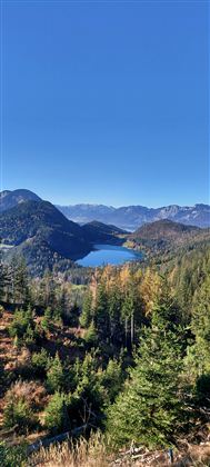 A picturesque mountain landscape with a clear lake in the middle. Surrounded by green forests and blue sky.