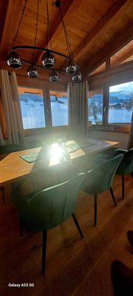 Ein gemütlicher Essbereich mit einem großen Tisch und modernen Stühlen. Das Fenster bietet einen schönen Blick auf die verschneite Landschaft.