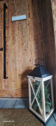 Eine gemütliche Ecke mit einer Holzwand und einer dekorativen Laterne. Die Laterne enthält Pflanzen und steht auf einem Holzfußboden.