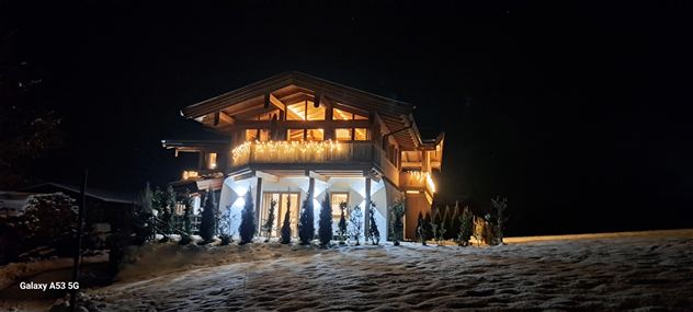 Ein schön beleuchtetes Holzhaus in der Nacht, umgeben von Schnee. Die warmen Lichter schaffen eine gemütliche Atmosphäre.