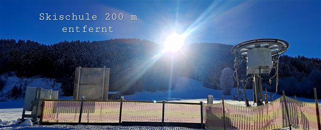 Ein klarer blauer Himmel über einem verschneiten Hang. Die Skischule ist 200 m entfernt.