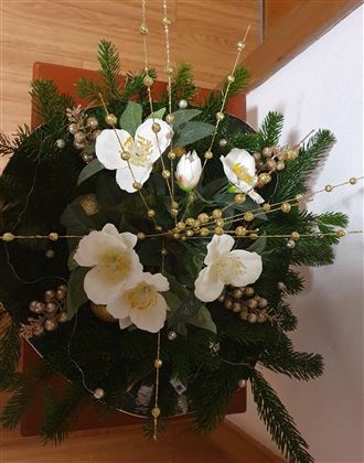 Ein dekorativer Blumenarrangement mit weißen Blumen und grünen Zweigen. Die Komposition enthält goldene Akzente und verleiht eine festliche Stimmung.