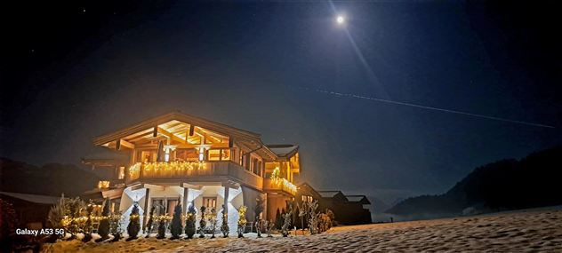 Ein gemütliches Haus bei Nacht, beleuchtet von warmen Lichtern. Der hell erleuchtete Mond steht am Himmel und schafft eine ruhige Atmosphäre.