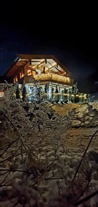 Ein wunderschönes, beleuchtetes Chalet bei Nacht, umgeben von Schnee. Die festliche Atmosphäre wird durch die Dekoration und die Lichter betont.