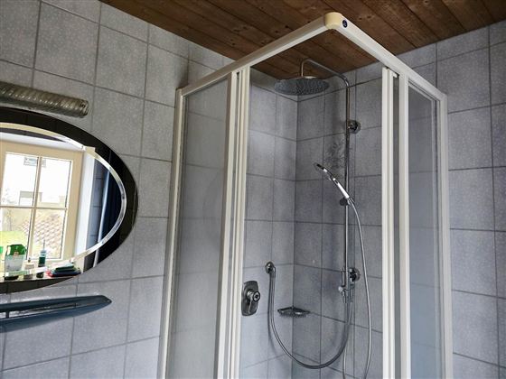 Eine moderne Duschkabine mit Glasschwenktüren steht in einem gefliesten Badezimmer. Ein runder Spiegel und eine praktische Ablage sind ebenfalls zu sehen.