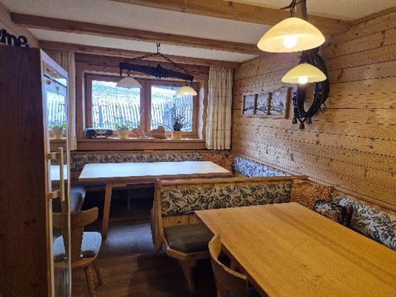 Ein gemütlicher Raum mit Holzwänden und mehreren Tischen. Die Fenster lassen viel Licht hereinf fallen und Pflanzen sorgen für eine einladende Atmosphäre.