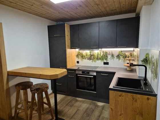 Eine moderne Küche mit dunklen Möbeln und Holzdetails. Im Hintergrund sind Pflanzenmuster an der Wand zu sehen.