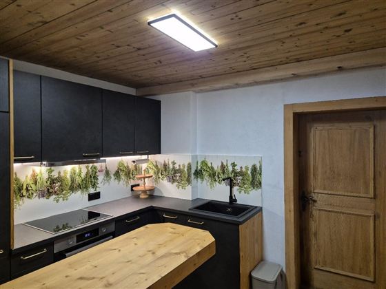 Eine moderne Küche mit schwarzen Schränken und einem großen Holztisch. An der Wand sind Pflanzenmuster dekoriert, die für eine frische Atmosphäre sorgen.