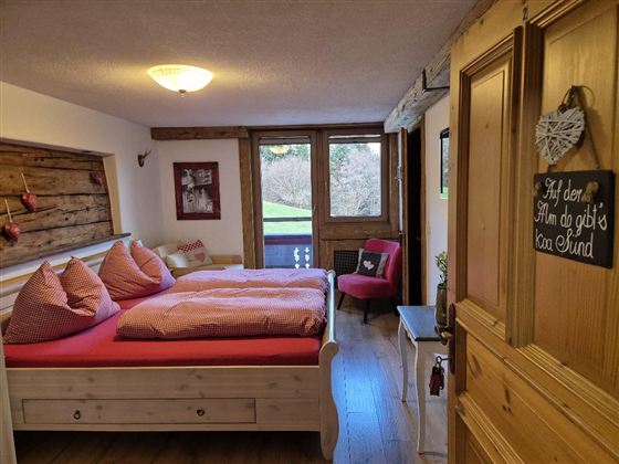 Ein gemütliches Schlafzimmer mit einem großen Bett und roten Kissen. Die Fenster bieten einen Blick auf die grüne Landschaft draußen.