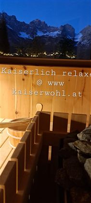 Ein gemütlicher Saunabereich mit Holzinterieur und Steinen. Im Hintergrund sind majestätische Berge bei Abenddämmerung zu sehen.