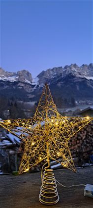 Ein leuchtender Weihnachtsstern aus Draht liegt auf einem Tisch. Im Hintergrund sind schneebedeckte Berge und ein klarer, blauer Himmel zu sehen.