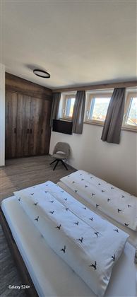 Ein modernes Schlafzimmer mit zwei Betten und einem Fernseher. Die Wände sind in warmen Holztönen gestaltet und die Fenster lassen viel Tageslicht herein.