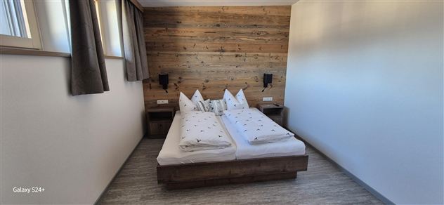 Ein gemütliches Schlafzimmer mit einem Doppelbett und rustikalem Holzdekor. Große Fenster lassen viel Tageslicht herein.