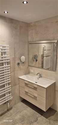 Ein modernes Badezimmer mit einem Holzwaschtisch und einem großen Spiegel. An der Wand befindet sich ein Handtuchwärmer.