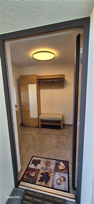 Ein heller Eingangsbereich mit einem Möbelstück für Garderobe und einem Platz zum Sitzen. Der Boden ist mit einem Teppich dekoriert.