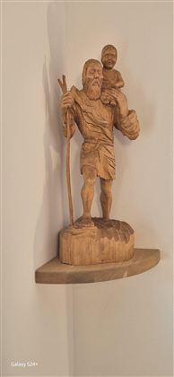 Eine Holzskulptur eines Mannes mit einem Kind auf der Schulter. Der Mann hält einen Gehstock und steht auf einem kleinen Regal.