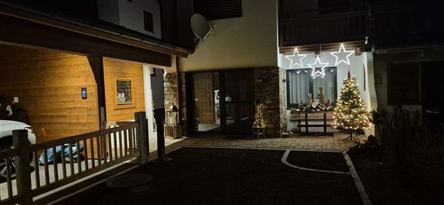 Ein festlich dekorierter Eingangsbereich eines Hauses mit Weihnachtsbaum und Lichtern. Die Umgebung ist nachts beleuchtet und schafft eine gemütliche Atmosphäre.