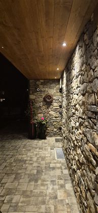 Ein schmaler, gepflasterter Weg führt entlang einer steinernen Wand. Die Beleuchtung und die Pflanzen schaffen eine einladende Atmosphäre.