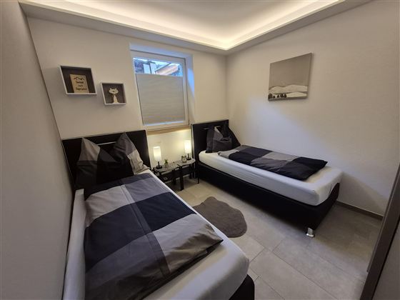 Ein modernes Schlafzimmer mit zwei Einzelbetten. Die Einrichtung ist schlicht und in neutralen Farben gehalten.