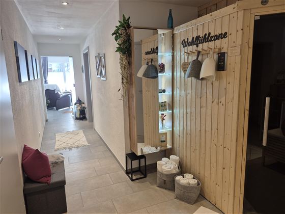 Ein einladender Flur mit hellen Wänden und einem Holzbereich. Rechts ist eine Wellnesszone mit Dekoration und einer Ruhebank.