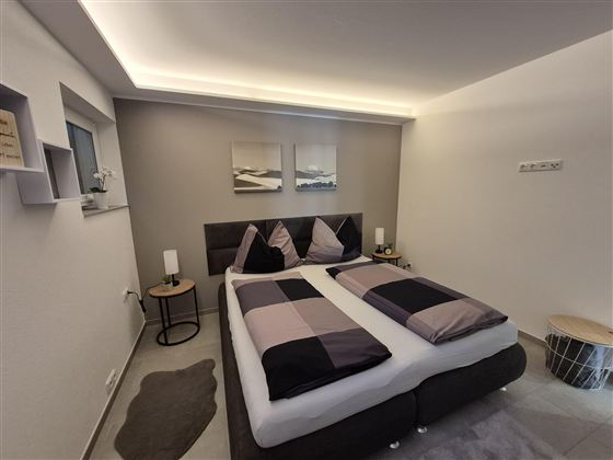 Ein modernes Schlafzimmer mit einem Doppelbett und stilvollen Kissen. Die Wände sind in neutralen Farben gehalten, und es gibt sanfte Beleuchtung.