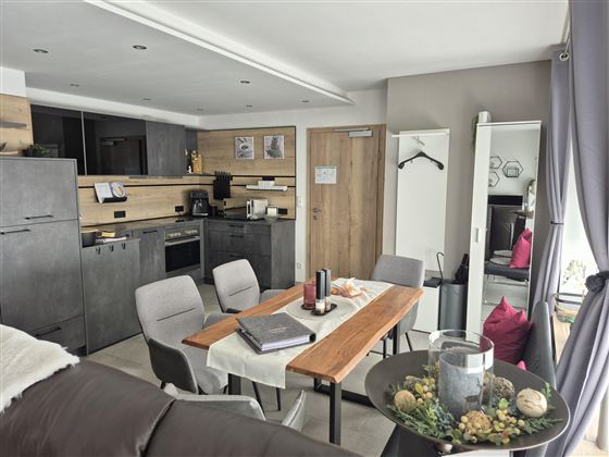 Ein modernes Wohnzimmer mit offener Küche. Der Tisch ist gedeckt und es gibt gemütliche Sitzgelegenheiten.