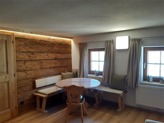 Pohodlná jídelna s kulatým stolem a dřevěnými lavicemi. Stěny jsou obloženy rustikálními dřevěnými panely a okna zajišťují hodně denního světla.