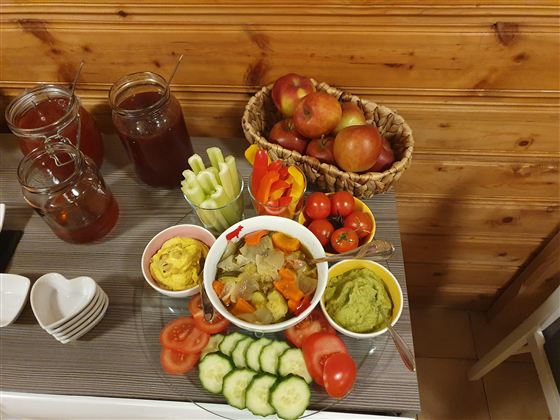 Ein Tisch mit verschiedenen frischen Lebensmitteln. Es gibt Gemüse, Dips und Obst in bunten Schalen.