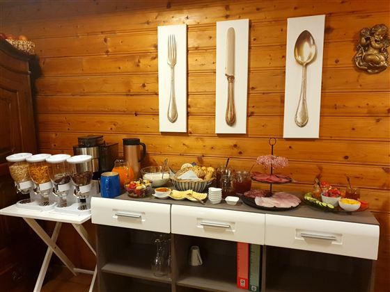 Ein liebevoll angerichtetes Buffet mit verschiedenen Speisen und Getränken, ergänzt durch dekorative Wandbilder von Besteck. Die Holzvertäfelung sorgt für eine gemütliche Atmosphäre.
