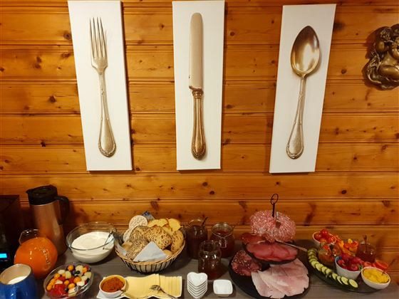 Ein reichhaltiges Frühstücksbuffet mit verschiedenen Köstlichkeiten. Im Hintergrund hängen Bilder von Besteck an einer Holzwand.