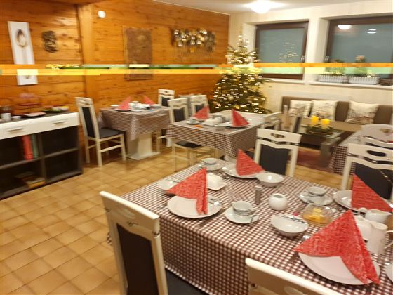 Ein gemütlich dekorierter Frühstücksraum mit mehreren Tischen. Die Tische sind mit roten Servietten und Geschirr gedeckt, und ein Weihnachtsbaum steht im Hintergrund.
